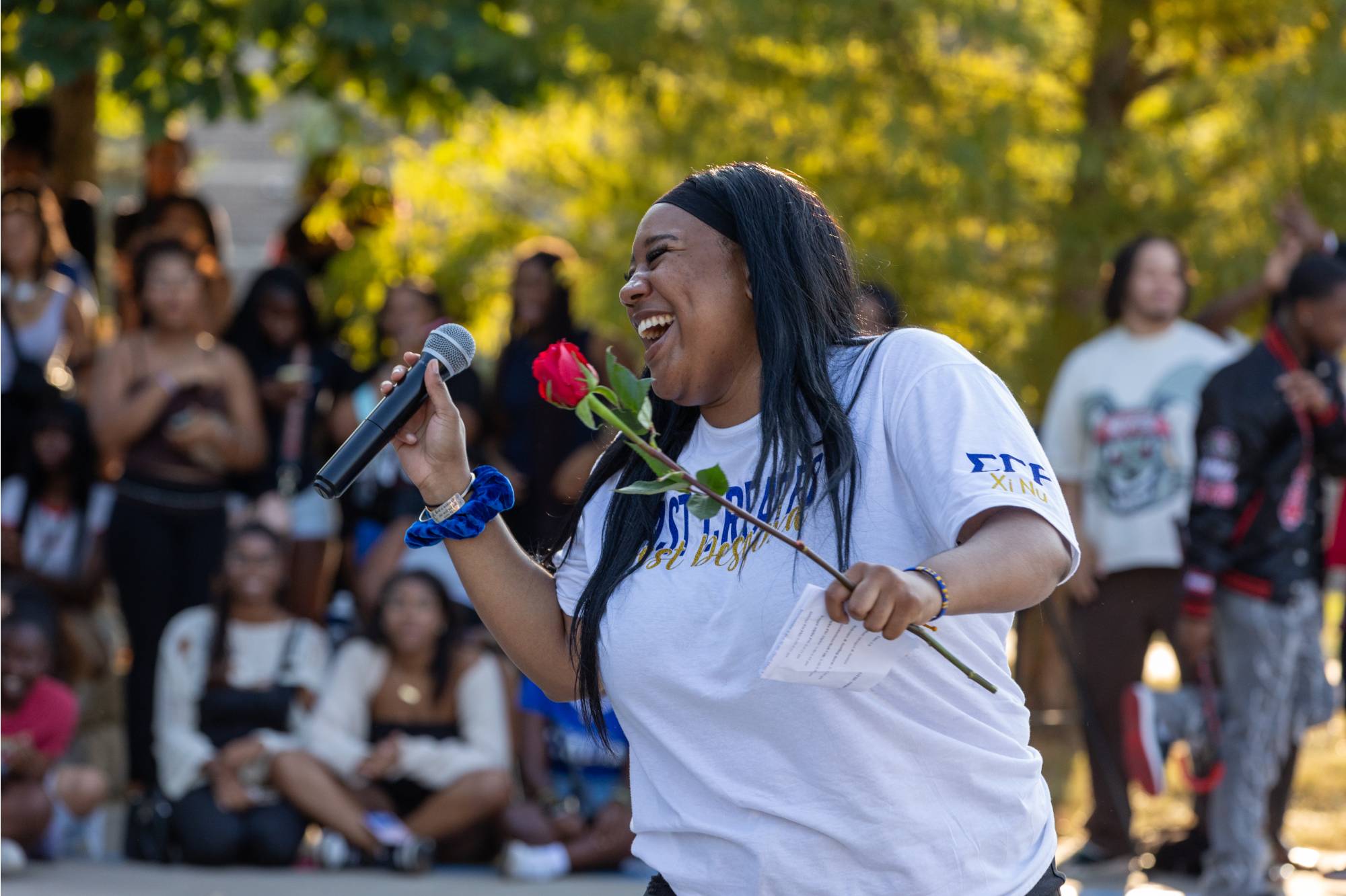A student laughs while holding a microphone and a red rose at the NPHC Yard Show